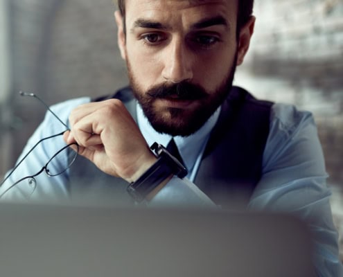 Professionista con gli occhiali in mano che osserva attentamente lo schermo del computer
