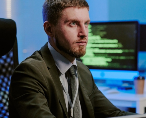 Professionista al computer con più monitor alle spalle in un ambiente di lavoro IT